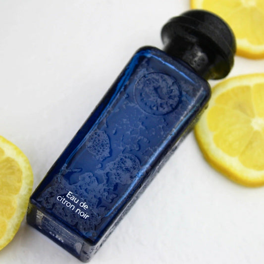Blue bottle labeled 'Eau de citron noir' with lemon slices on a white background