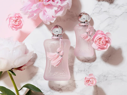 Two pink perfume bottles with decorative elements on a marble surface with flowers.
