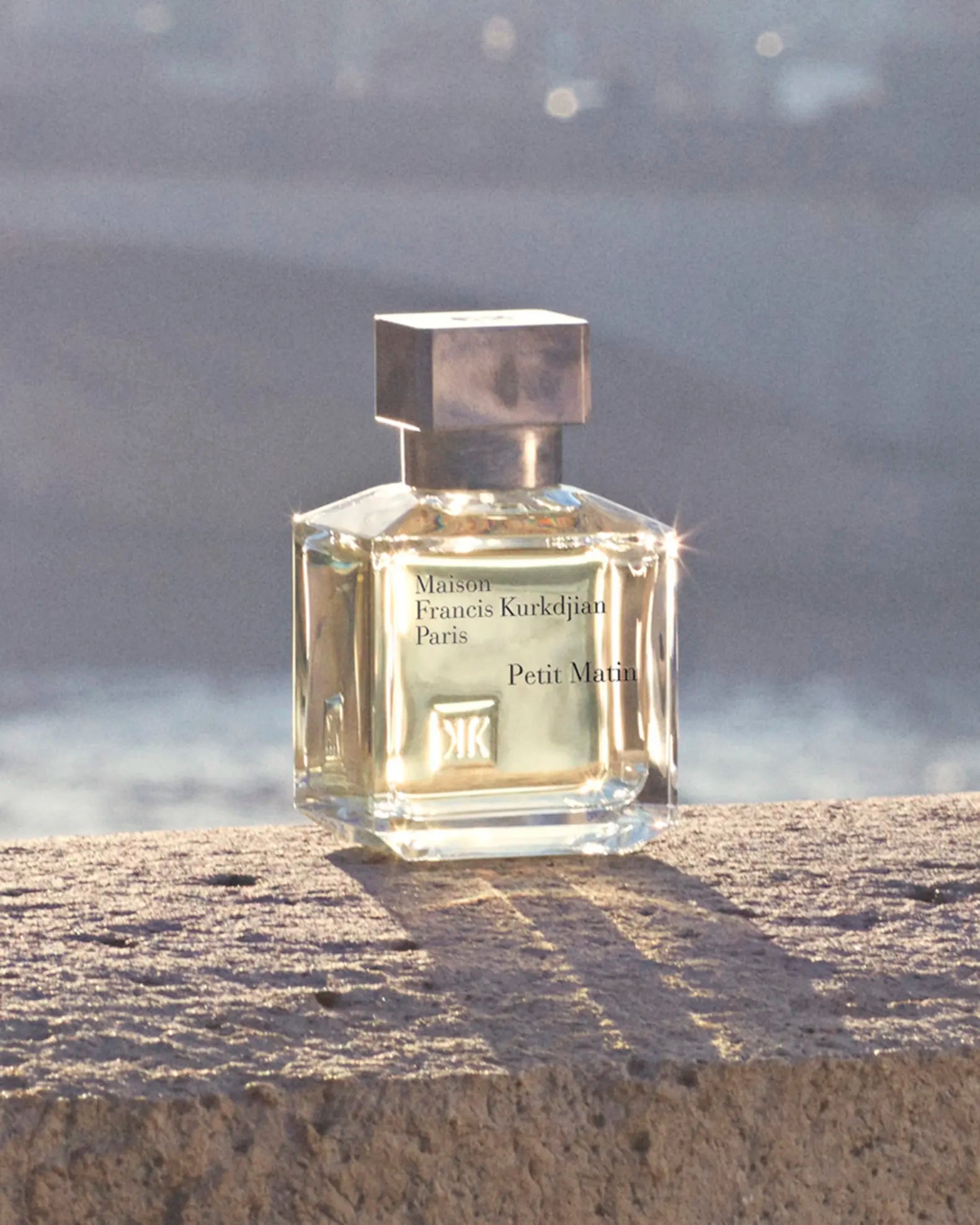 Perfume bottle labeled 'Petit Matin' by Maison Francis Kurkdjian on a stone surface with a misty background.