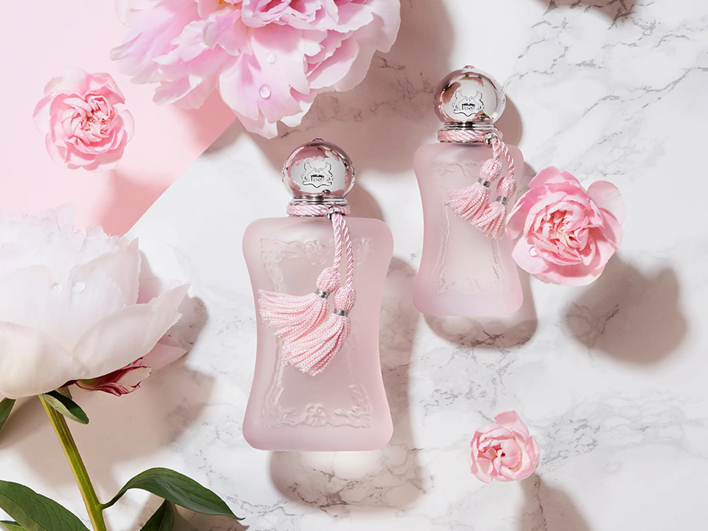 Two pink perfume bottles with decorative elements on a marble surface with flowers.