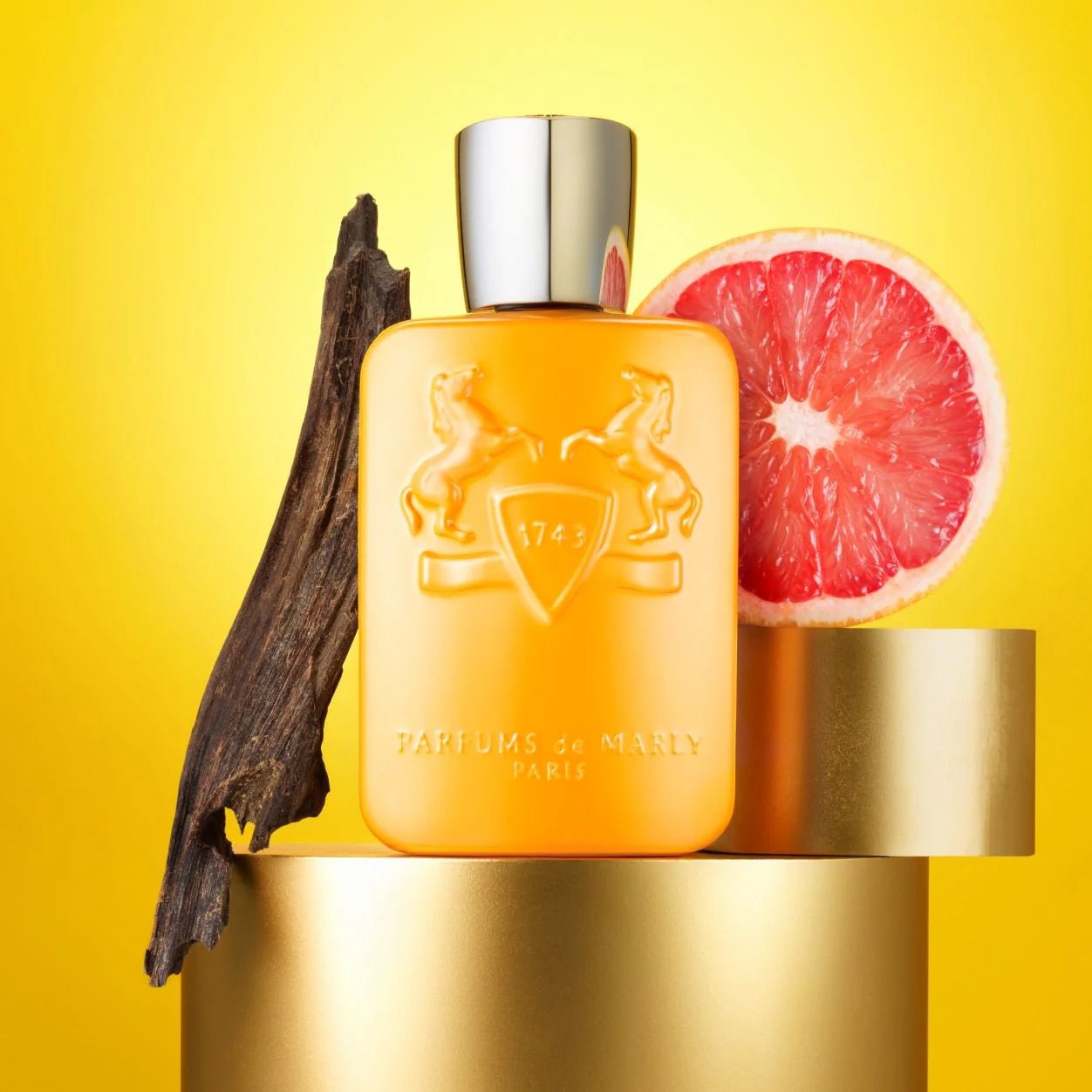 Perfume bottle with vanilla bean, grapefruit, and gold container on a yellow background